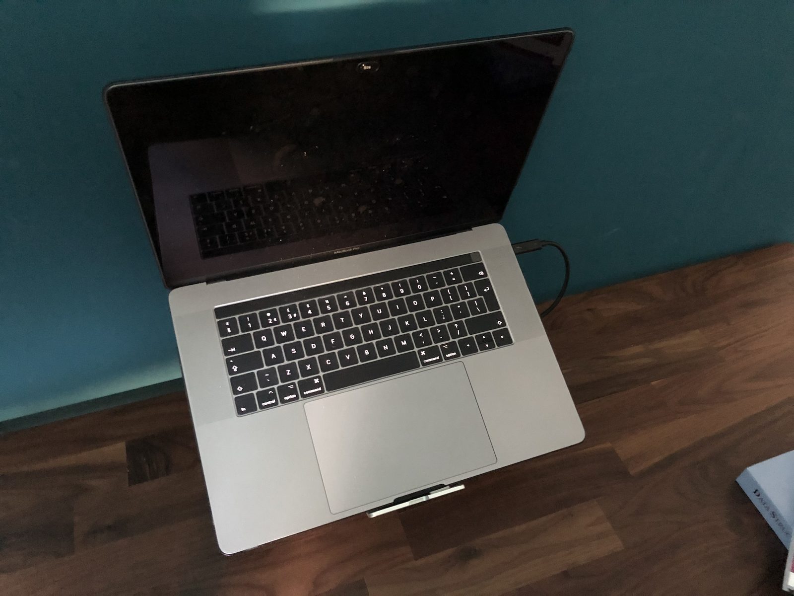 A space grey 15-inch MacBook Pro with a Touch Bar, open on a laptop stand.