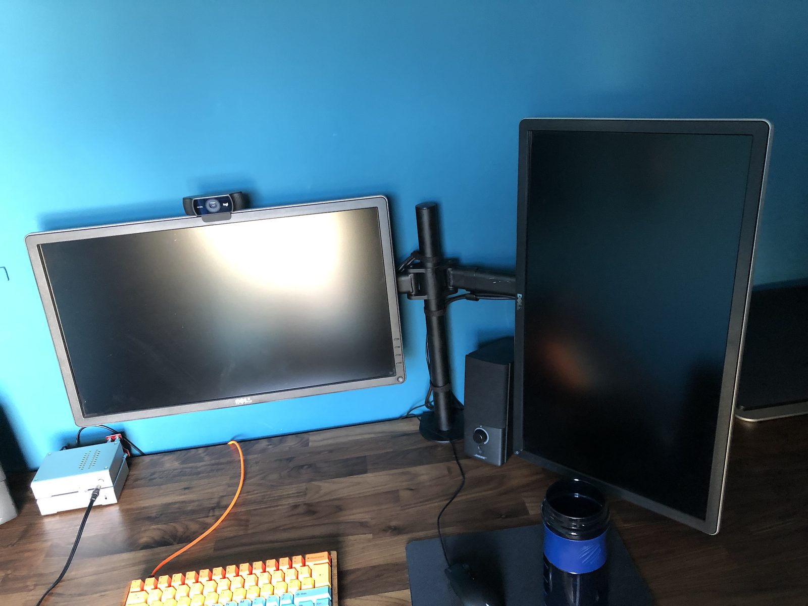 Two Dell monitors on a single arm, one landscape with a Logitech webcam on top and one turned to portrait, with a small Bose speaker between them.
