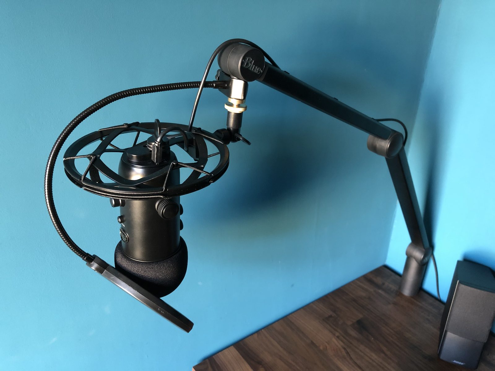 A black Blue Yeti microphone in a shock mount with a pop filter, on a Blue boom arm clamped to the desk.