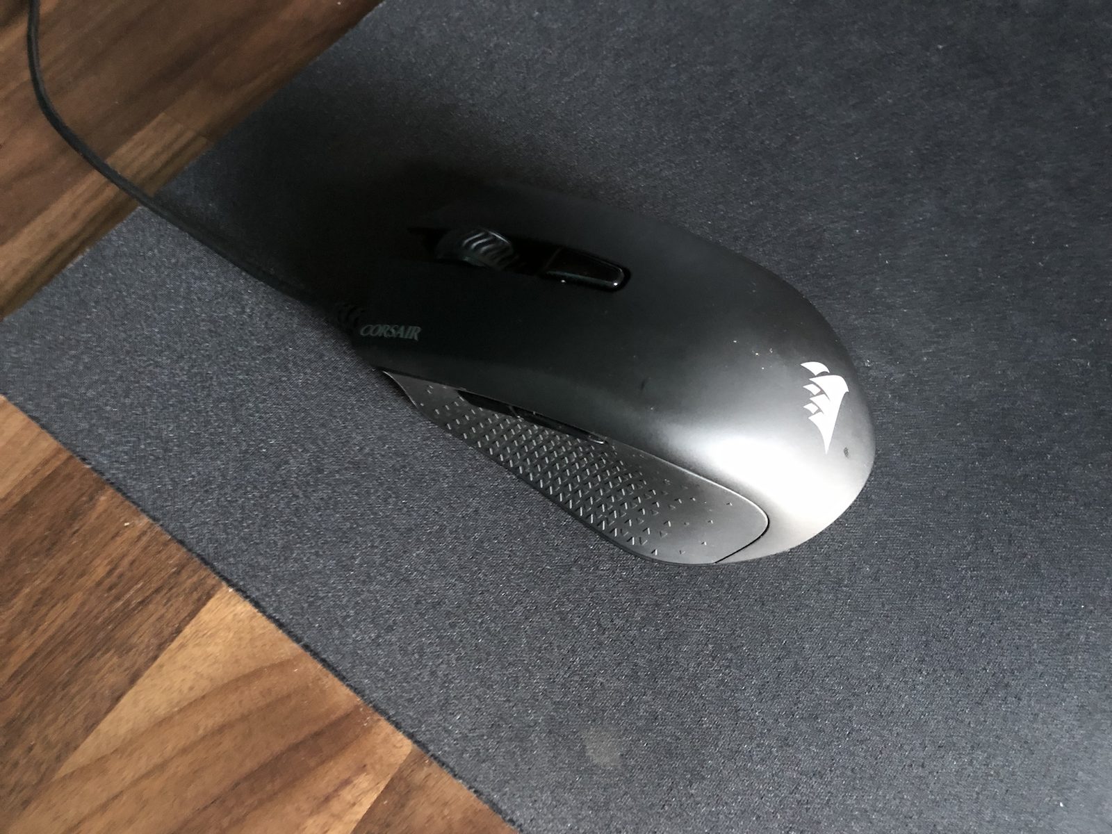 A black Corsair gaming mouse on a dark grey fabric mouse mat.